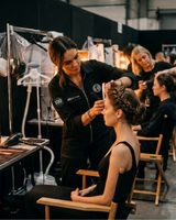 Hairdresser styling a model's hair in a busy salon setting with other staff and clients.