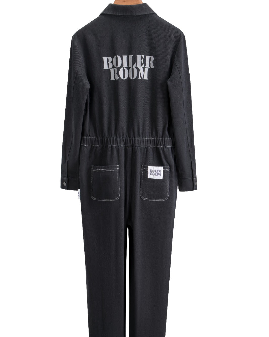 Black Foil Style Boiler Room jumpsuit shown from the back on a wooden hanger, featuring 'BOILER ROOM' printed across the shoulders and a logo patch on the back pocket, against a white background
