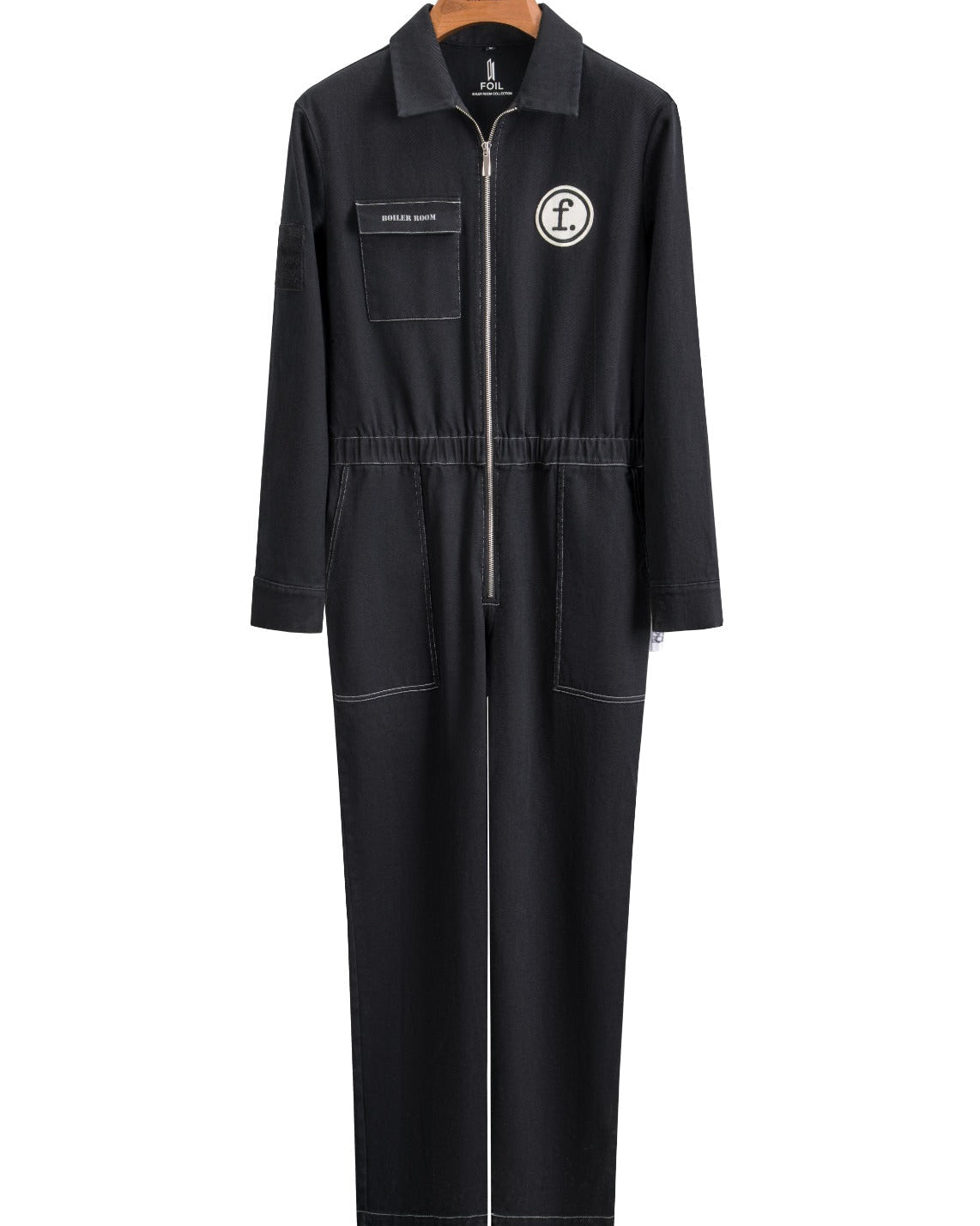 Black Foil Style Boiler Room jumpsuit shown from the front on a wooden hanger, featuring a chest pocket, front zipper, and circular logo patch, against a white background