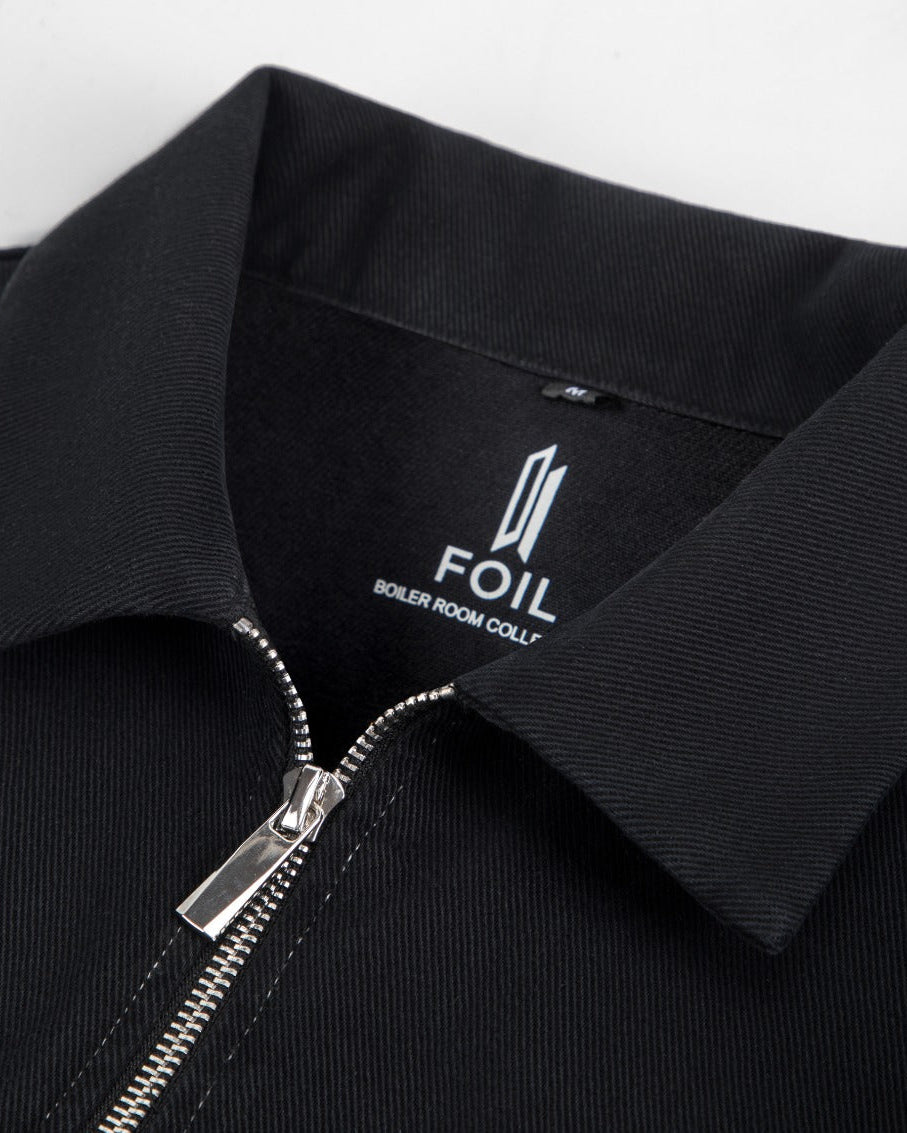 Close-up of a black collared zip-front jacket or overshirt with a silver zipper and a visible neck label reading FOIL.