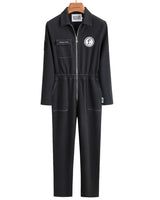 A black long-sleeve jumpsuit with a front zipper, chest pocket, and a circular white logo on the left chest, hanging on a wooden hanger against a plain white background.
