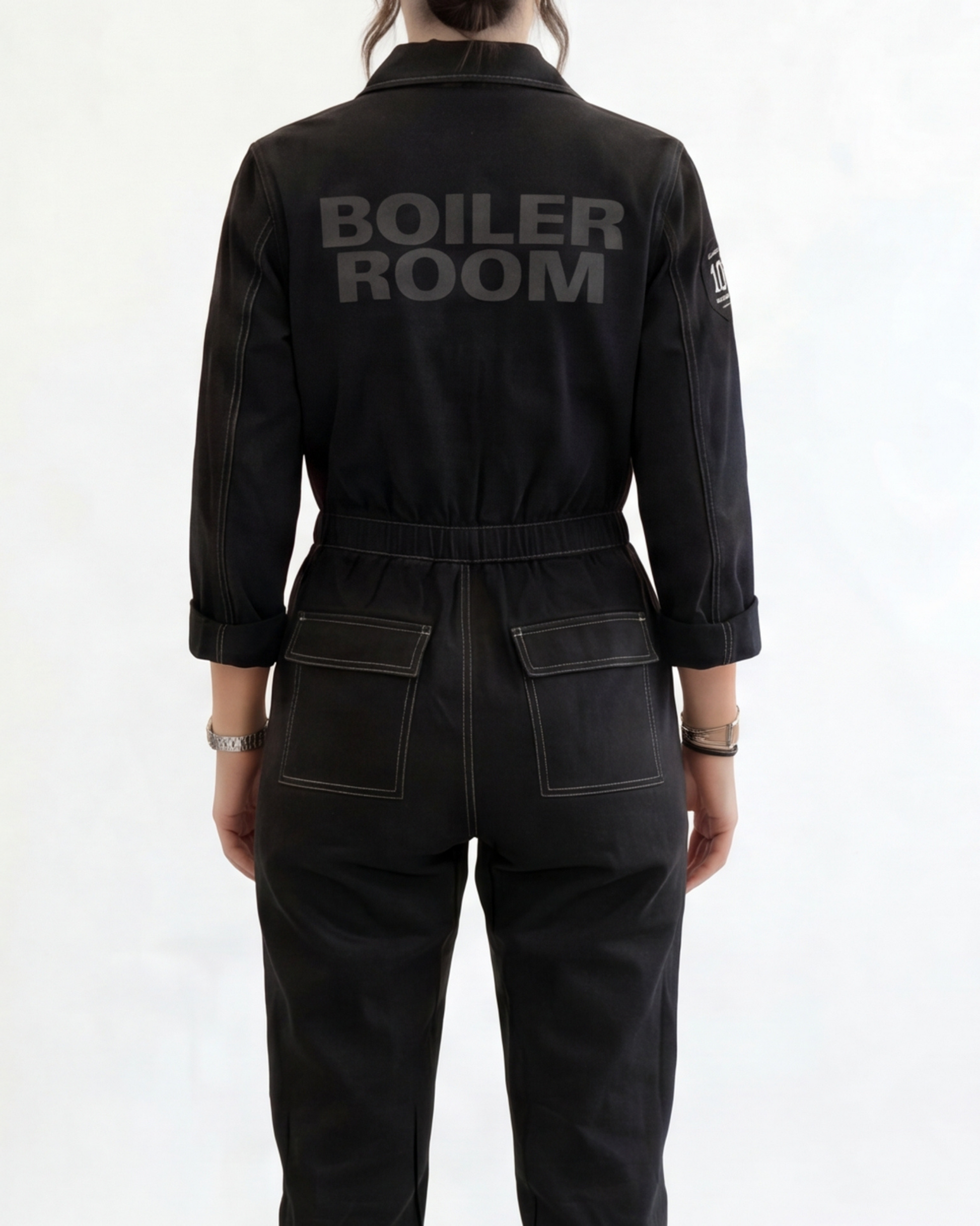 Person wearing a black boiler suit with 'BOILER ROOM' branding on a white background