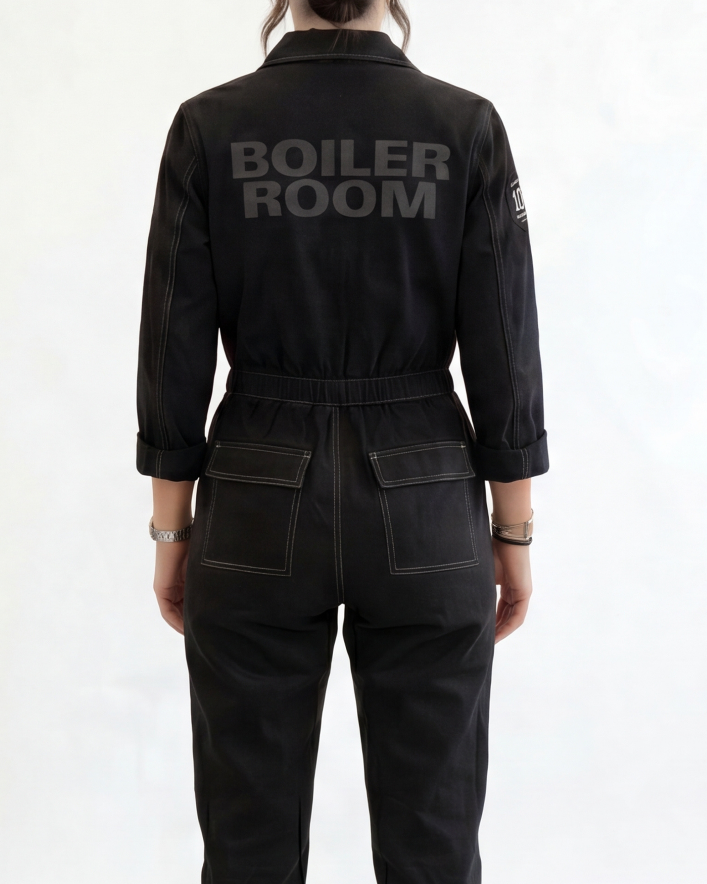 Person wearing a black boiler suit with 'BOILER ROOM' branding on a white background
