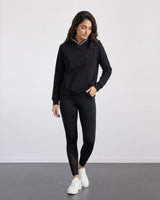 Woman wearing a black hoodie and leggings with white sneakers on a plain background