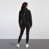Person wearing a black hoodie and leggings with a visible brand logo on the back, standing against a plain white background.