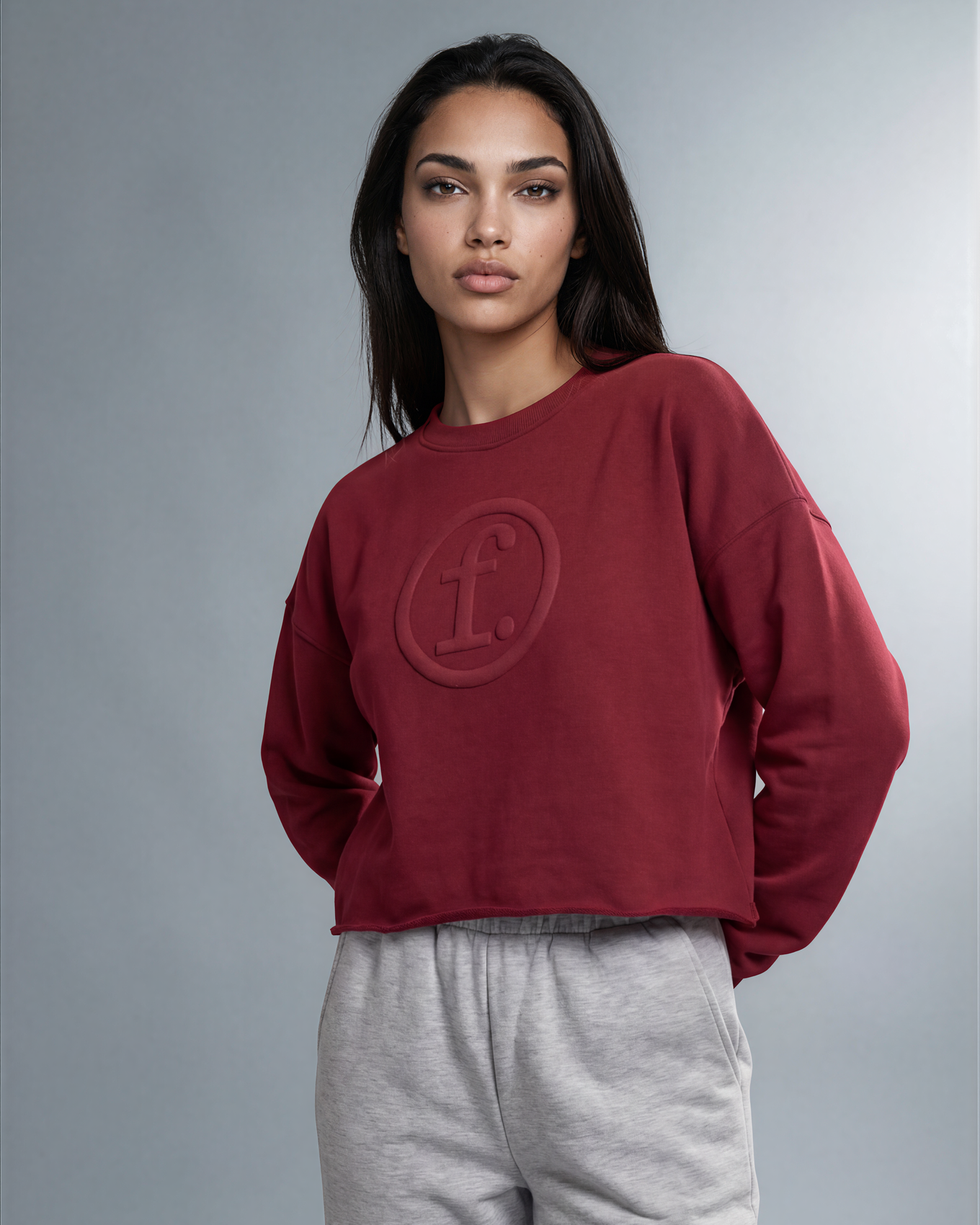 Woman wearing a red sweatshirt with a logo and gray pants on a gray background