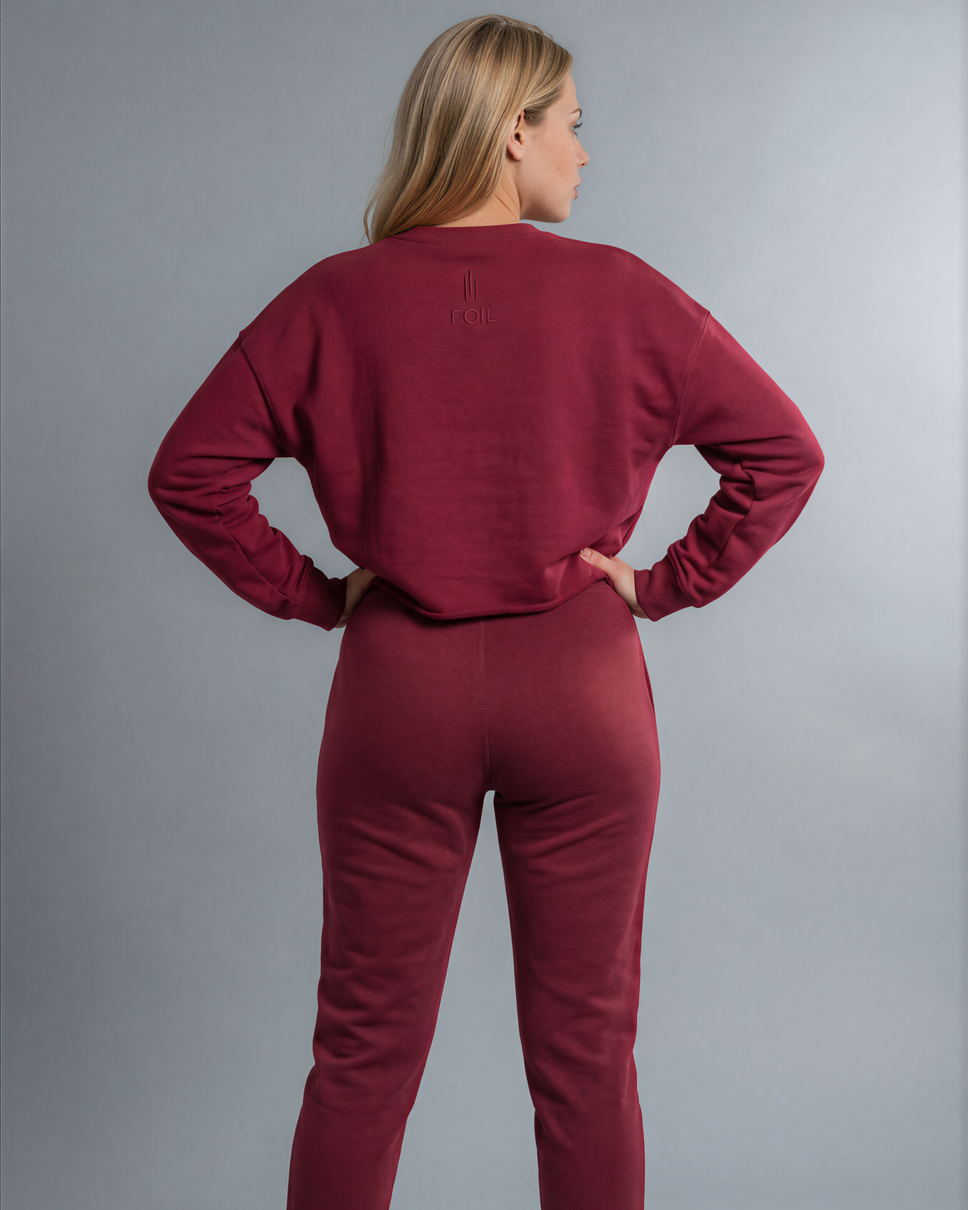 Person wearing a maroon tracksuit against a gray background