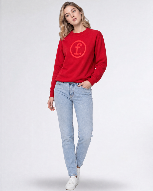 A woman modeling a bright red crewneck sweatshirt with a tonal red circular 'f' logo on the chest, paired with light-wash blue jeans and white sneakers, against a light gray studio background.
