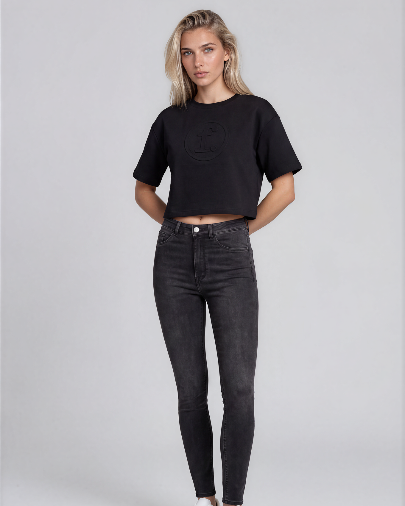 Woman wearing a black crop top and dark jeans on a plain background