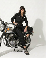 Person wearing a black outfit sitting on a motorcycle against a white background