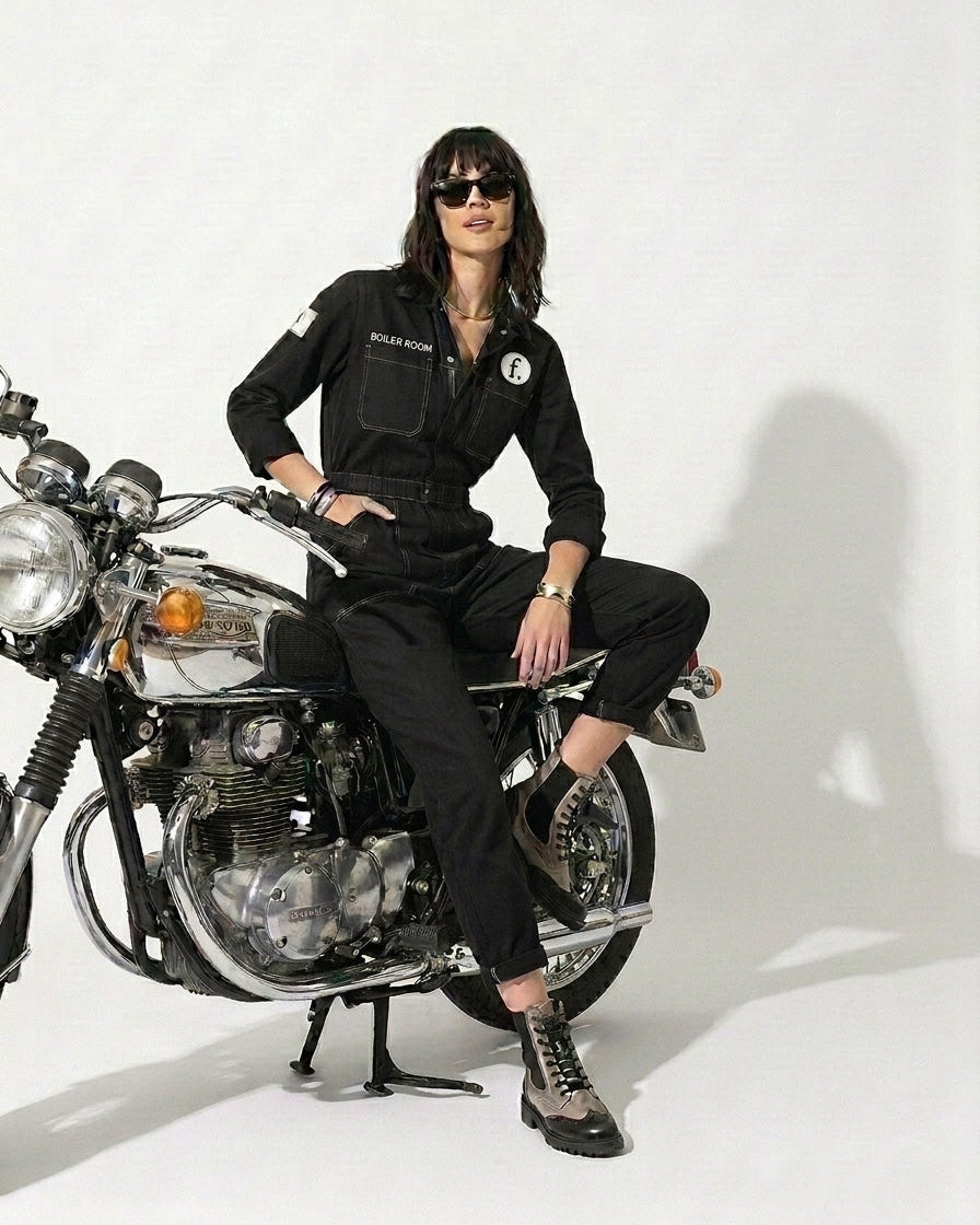 Person wearing a black outfit sitting on a motorcycle against a white background