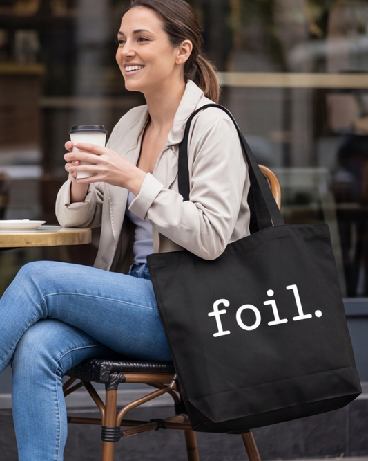 Woman sitting at an outdoor cafe holding a drink with a 'foil' bag.