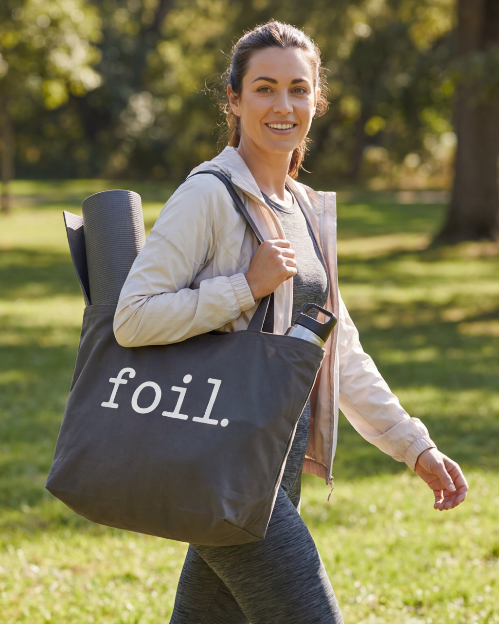 Woman carrying a tote bag with 'foil.' text in a park