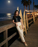 Woman standing on a wooden boardwalk by the ocean with surfboards, at night.