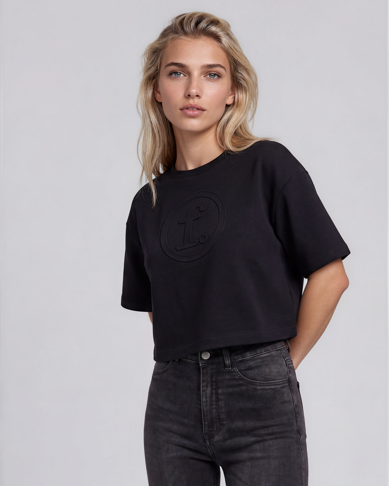 Woman wearing a black t-shirt and dark jeans on a light gray background