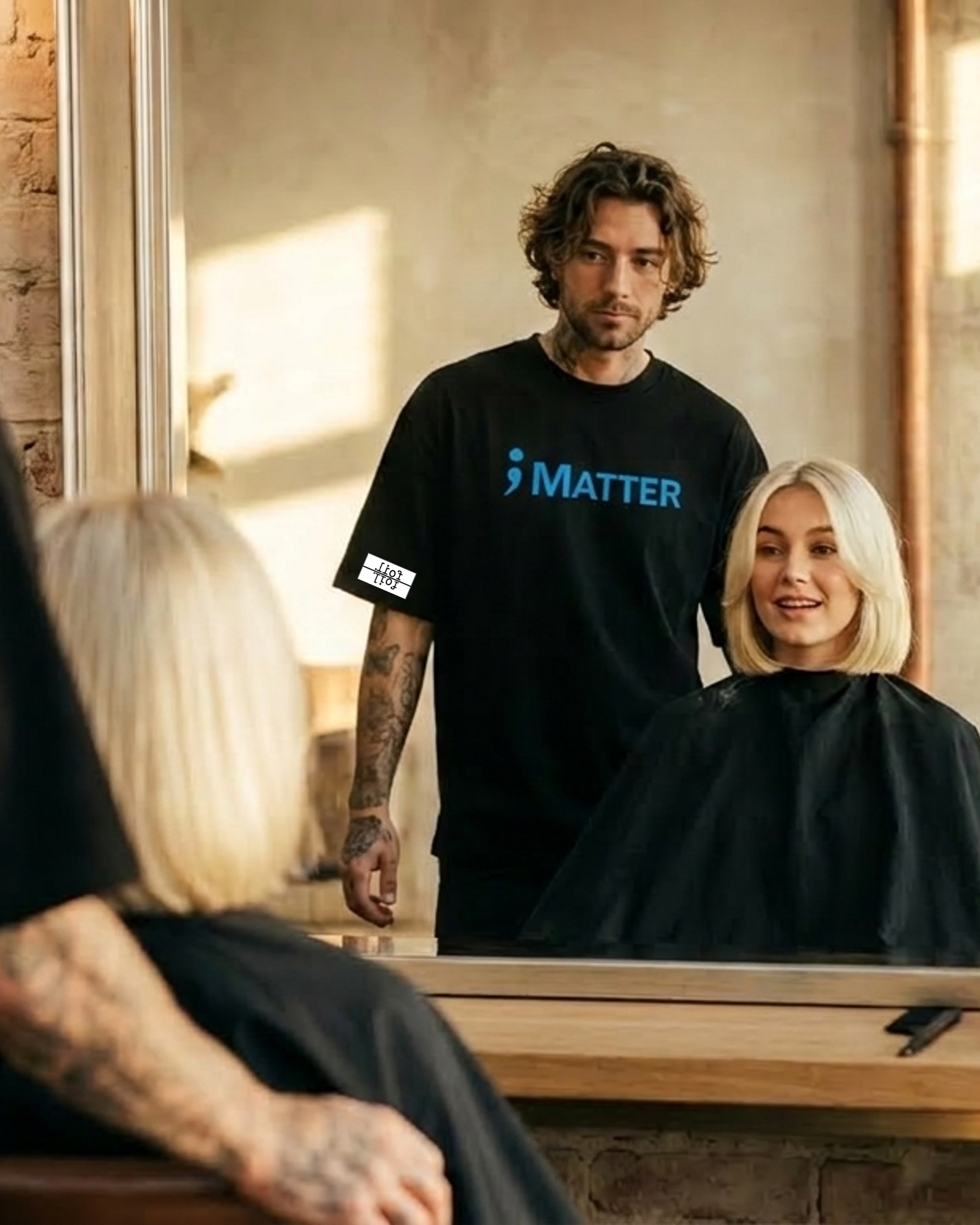 A man in a black barber-style shirt with the blue 'MATTER' logo stands in a salon mirror while reflecting a blonde woman seated under a black salon cape. Another person is partially visible in the foreground.