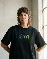 Person wearing a black t-shirt with colorful text in front of a window.