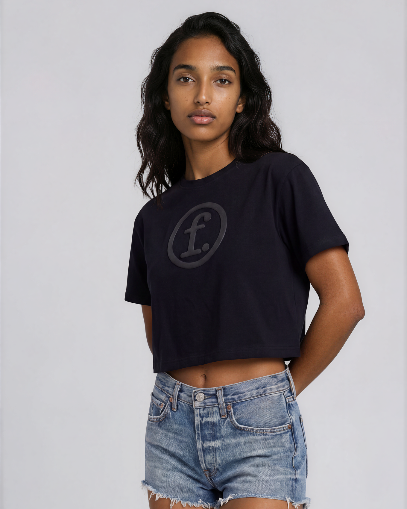 Woman wearing a black t-shirt with a logo and denim shorts on a light gray background