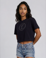 Woman wearing a black t-shirt with a logo and denim shorts on a light gray background