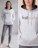 A woman wearing a light heather gray hoodie with 'foilstyle' printed across the chest in black and metallic gold. The image is a split-screen composite showing a full-body view on the left and a close-up of the chest print on the right.